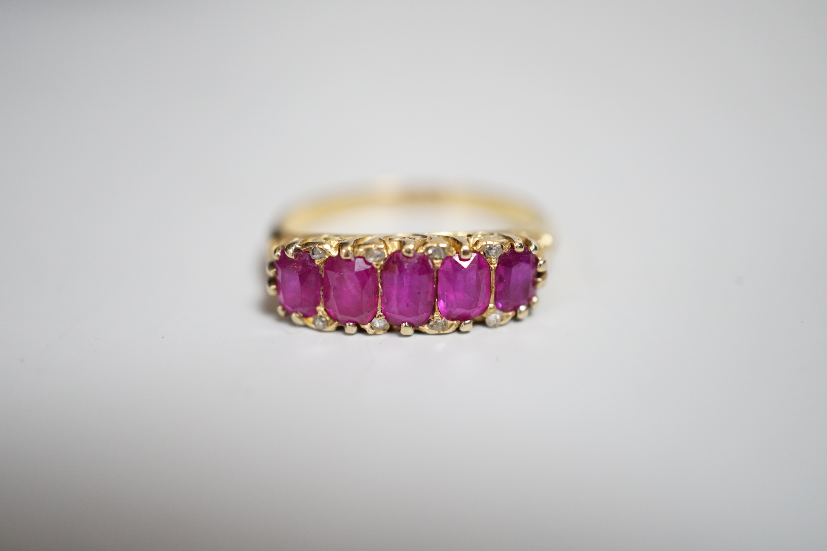 An early to mid 20th century 18ct and graduated five stone ruby set half hoop ring, with diamond chip spacers, size L, gross weight 3.5 grams.